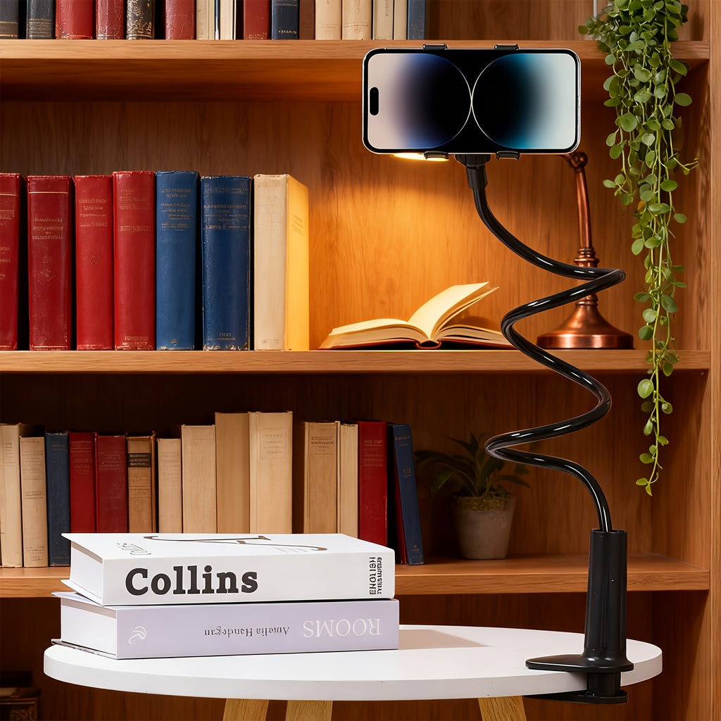 Black flexible gooseneck phone and tablet holder with a clamp base, holding a phone on a white table.